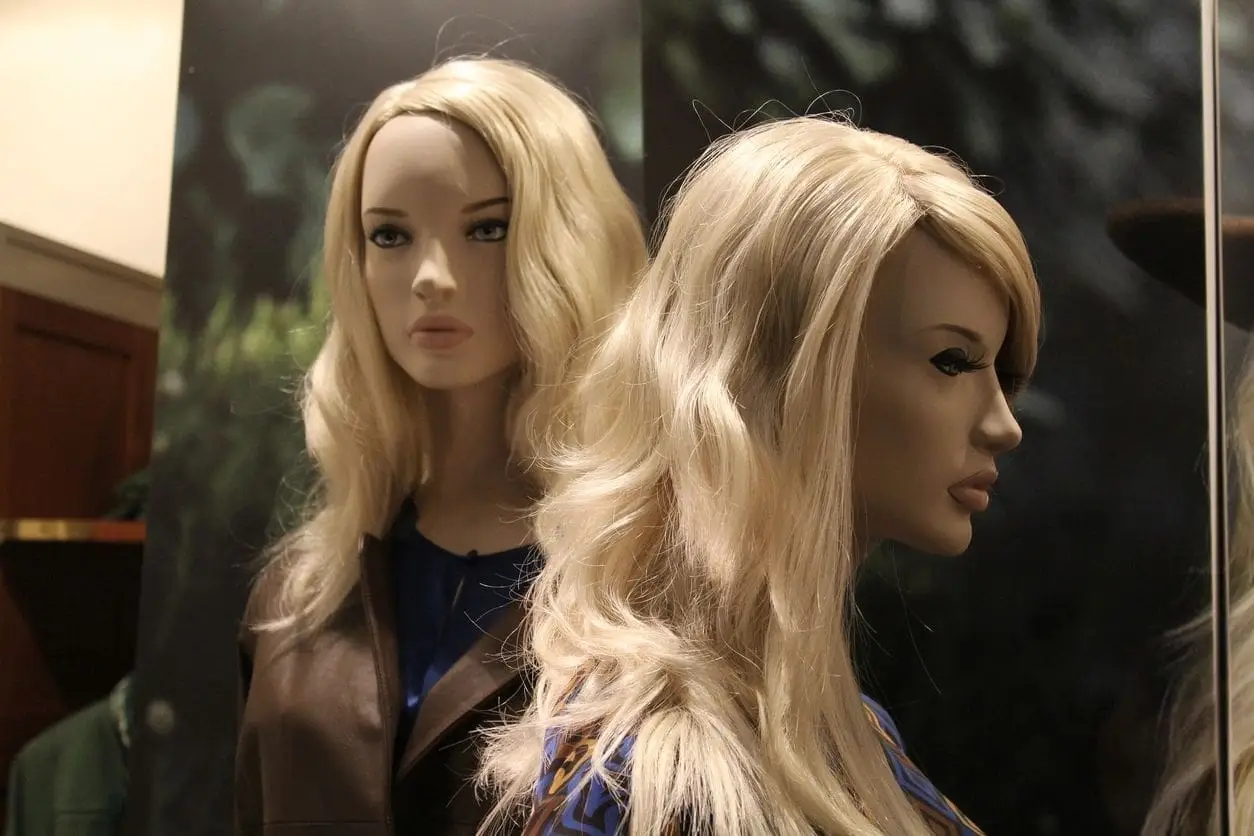 A woman 's face and head in the mirror of a mannequin.